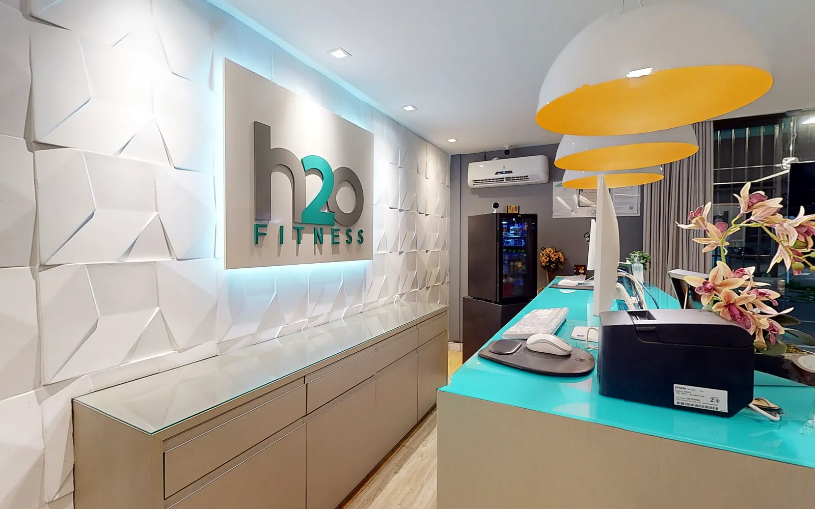 Recepção da H2O Fitness com logo iluminado e balcão turquesa